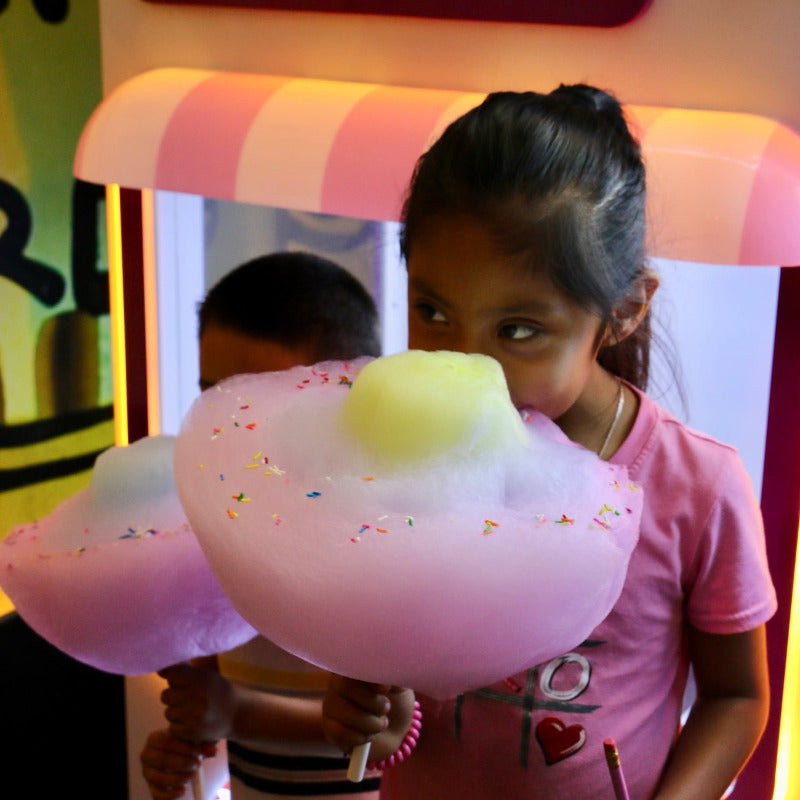 two young children eating large cotton candy flowers with sprinkles on top, made by a Sweet Robo Model VX Cotton Candy Vending Machine