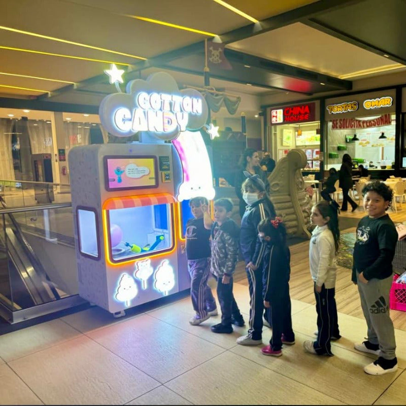 a line of children waiting for cotton candy to be made by a Sweet Robo Model VX Cotton Candy Vending Machine that is set-up in a mall food court