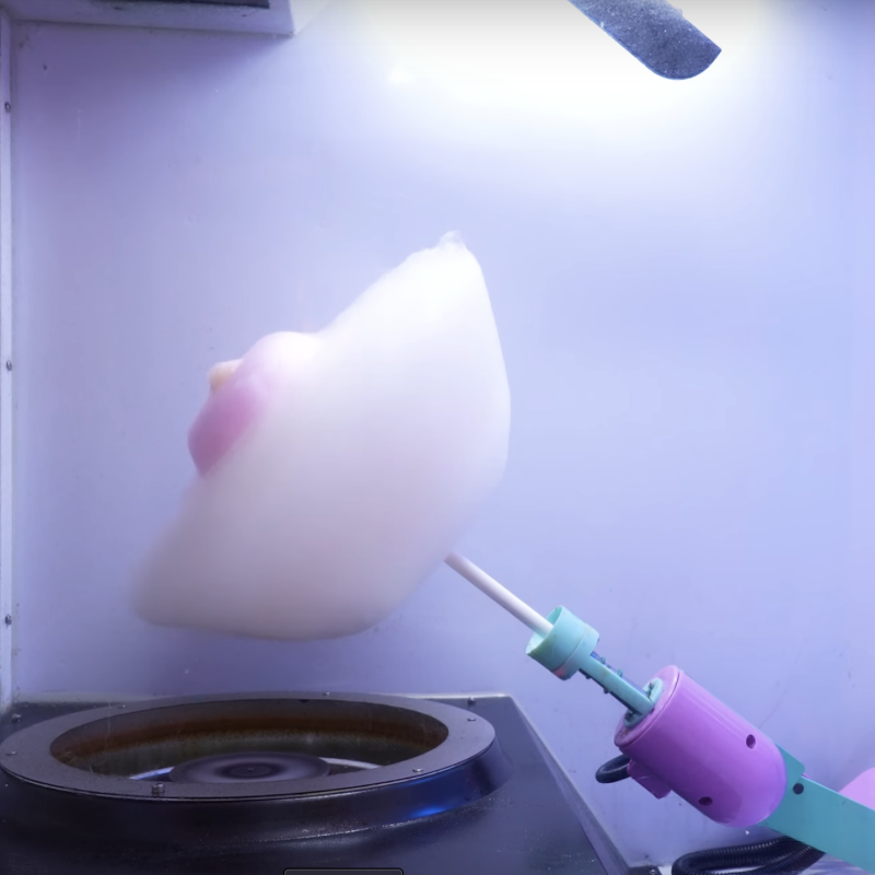 picture of brightly colored robot arm with an almost finished cotton candy flower on it, inside a Sweet Robo Model VX Cotton Candy Vending Machine